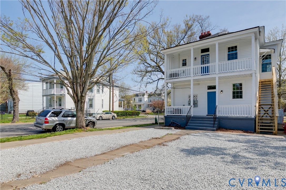 Two-story exterior with white lap siding, dual-level covered porches, external wooden staircase, and a dedicated gravel parking area
