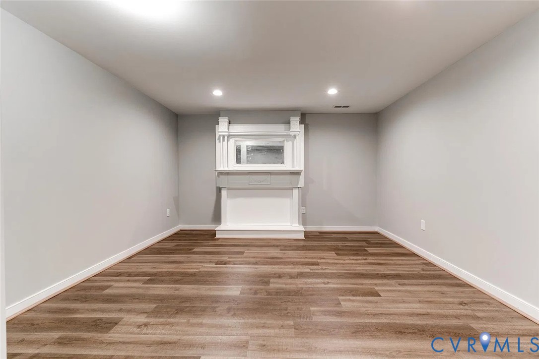 Interior space featuring wood-finish flooring, neutral wall paint, recessed lighting, and a white decorative mantel with a built-in mirror