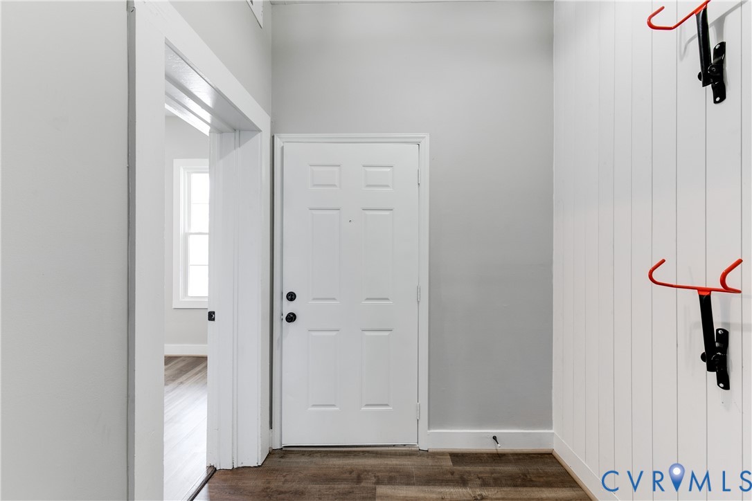 Entryway featuring wood-finish flooring, white vertical plank wall paneling, and a six-panel door