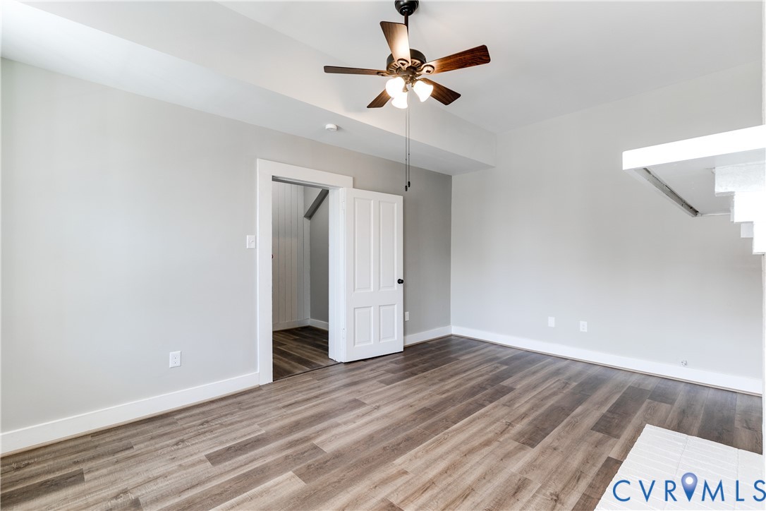 Interior space featuring wood-finish flooring, a multi-paneled door, recessed ceiling detail, and a ceiling fan with integrated lighting