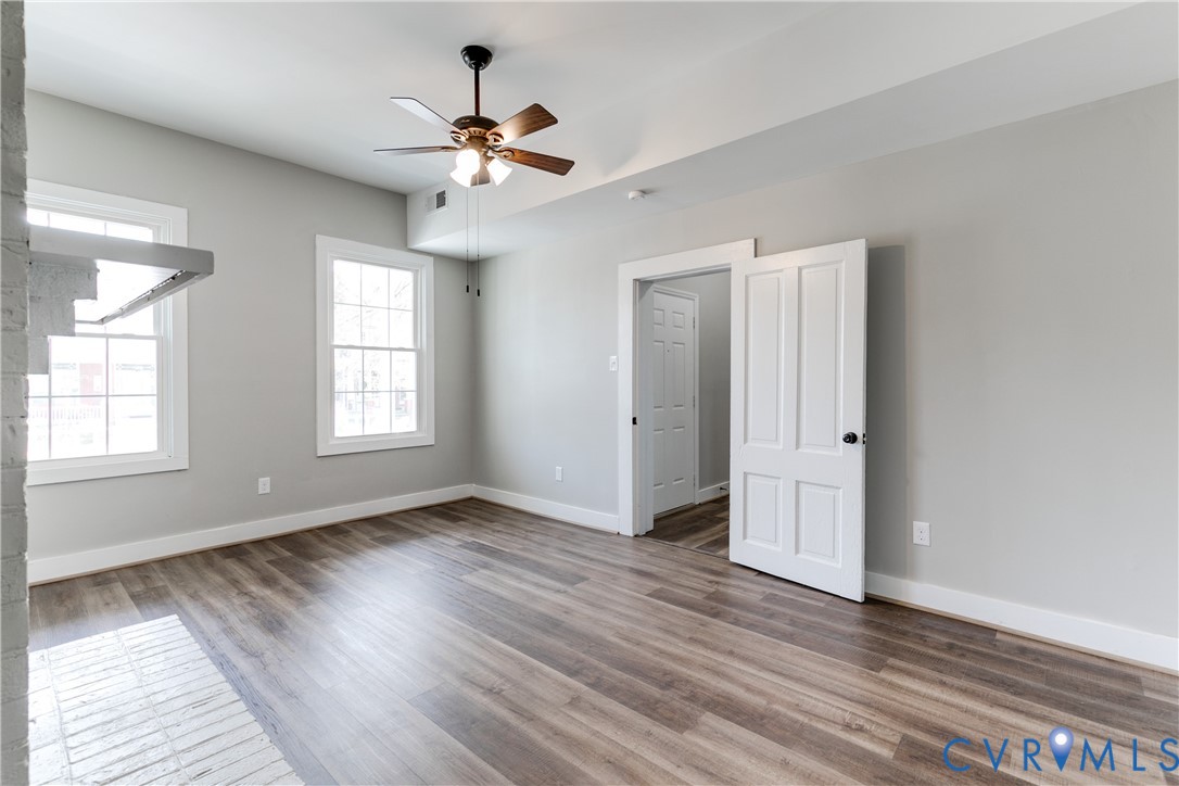 Interior space featuring wood-finish flooring, multi-pane windows, a central ceiling fan with integrated lighting, and white six-panel interior doors