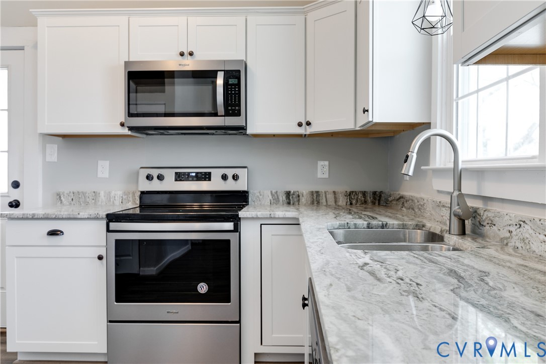 Kitchen featuring white shaker-style cabinetry, natural stone countertops, stainless steel appliances, a dual-basin undermount sink, and a high-arch pull-down faucet