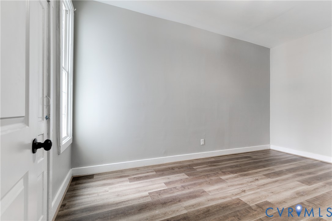 Neutral-toned walls, wood-finish flooring, and a multi-pane window with a black-finished handle, featuring a white paneled door with a matte black lever handle