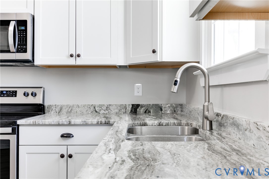 Shaker-style white cabinetry, natural stone countertops, stainless steel dual-basin under-mount sink, high-arc pull-down kitchen faucet, and stainless steel appliances
