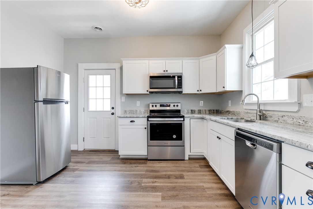 Kitchen featuring white cabinetry, stone-finish countertops, stainless steel appliances, wood-finish flooring, and a multi-pane glass door