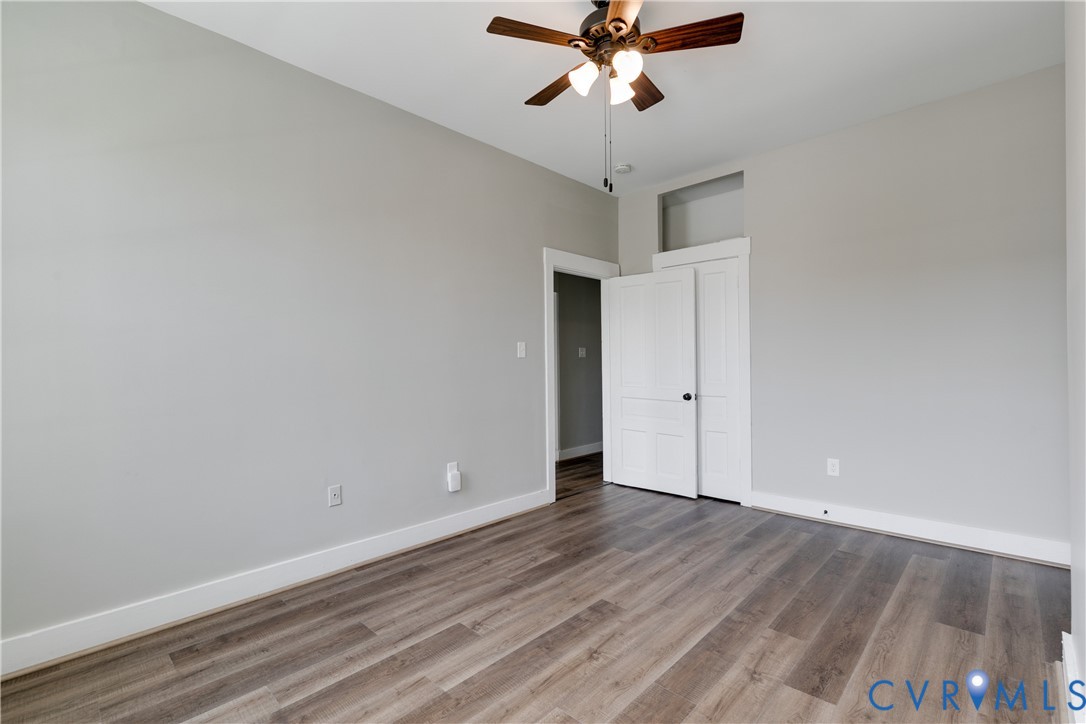 Room featuring wood-finish flooring, neutral wall paint, a ceiling fan with integrated lighting, and a door with a transom window