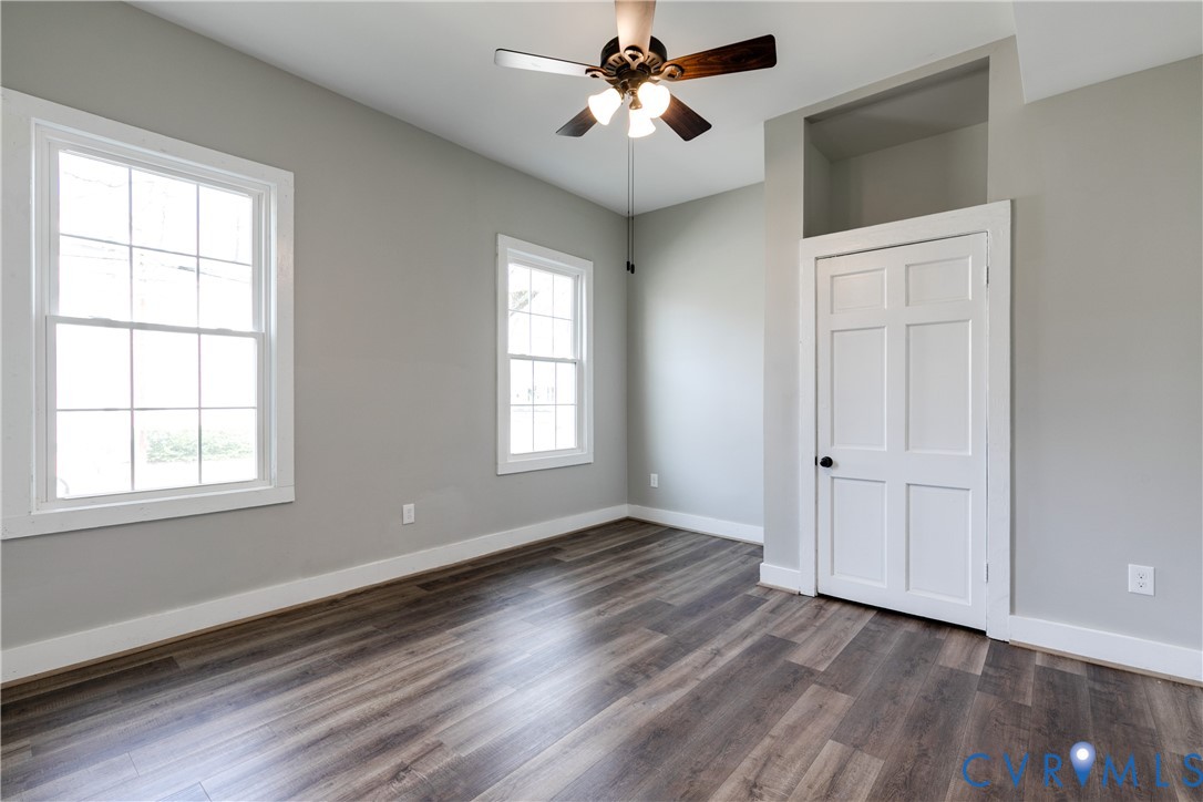 Interior space featuring wood-finish flooring, two multi-pane windows, a recessed wall niche above a six-panel door, and a ceiling fan with integrated lighting