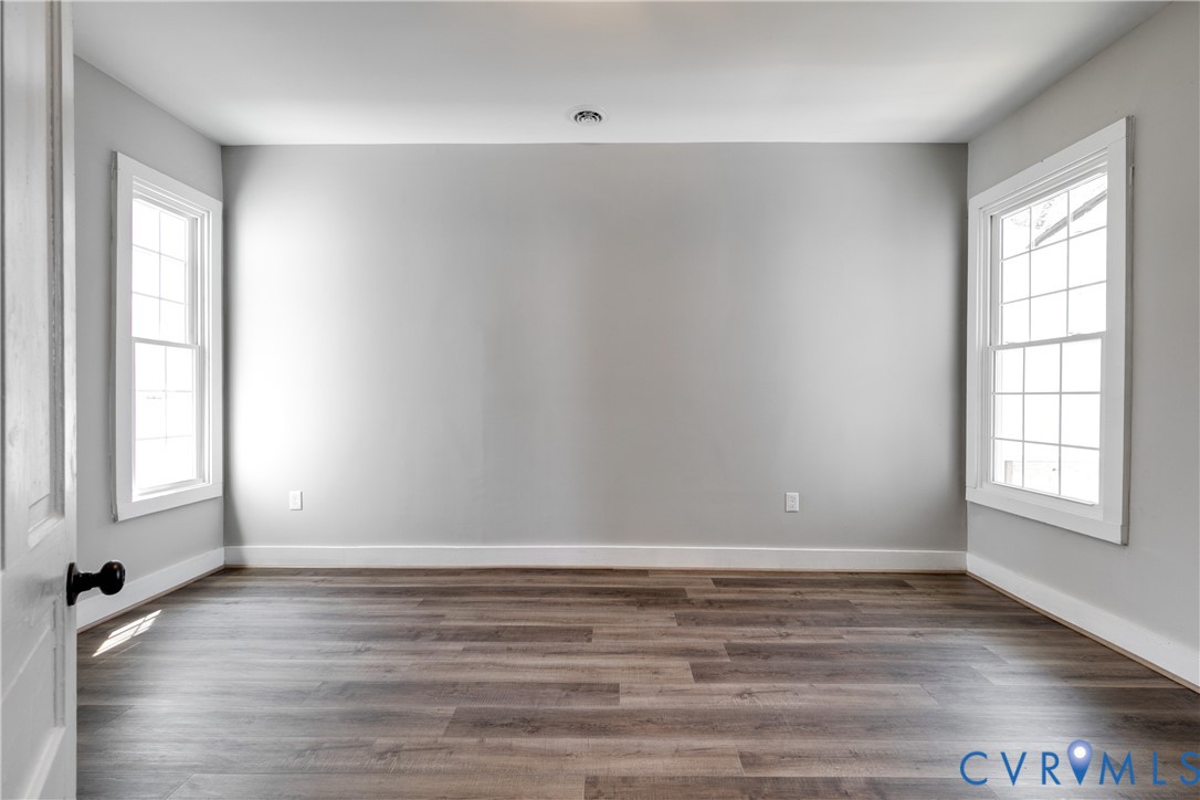 Interior room featuring wood-finish flooring, neutral wall paint, and dual windows with grid-pattern muntins