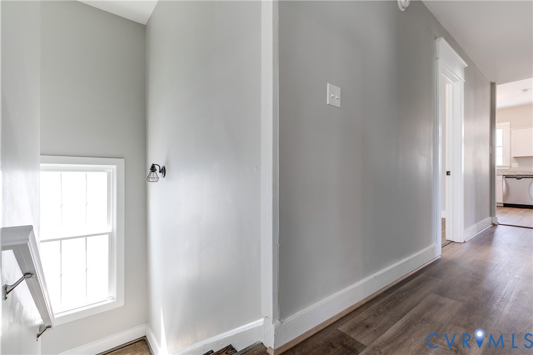 Wood-finish flooring, neutral wall tones, white door casings, and wall-mounted metal light fixture