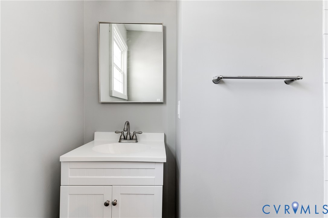 White vanity featuring an integrated countertop, stainless steel dual-handle faucet, rectangular wall-mounted mirror, and horizontal towel bar