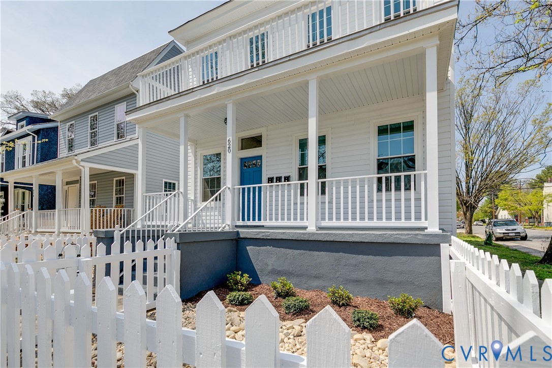 Two-story exterior featuring white horizontal siding, a covered front porch with a balcony, and a white picket fence