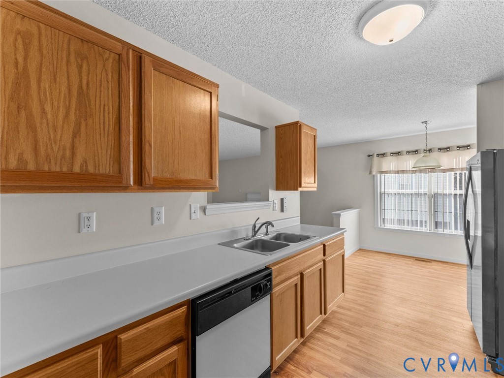 Kitchen featuring natural wood cabinetry, a solid surface countertop, a double-basin stainless steel sink, a built-in dishwasher, and wood-finish flooring