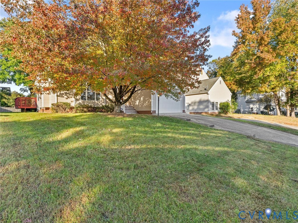 Exterior featuring light-colored siding, attached garage, paved driveway, elevated wooden deck, and mature deciduous trees