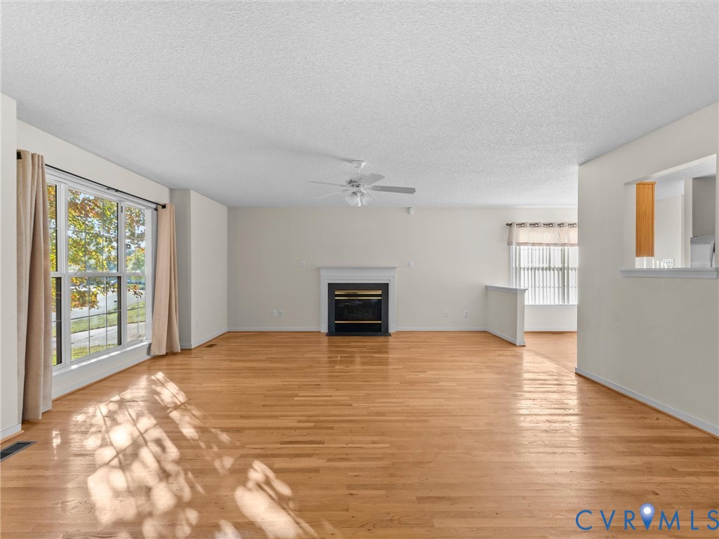 Living area featuring wood-finish flooring, a fireplace with a mantel, ceiling fan, and large windows