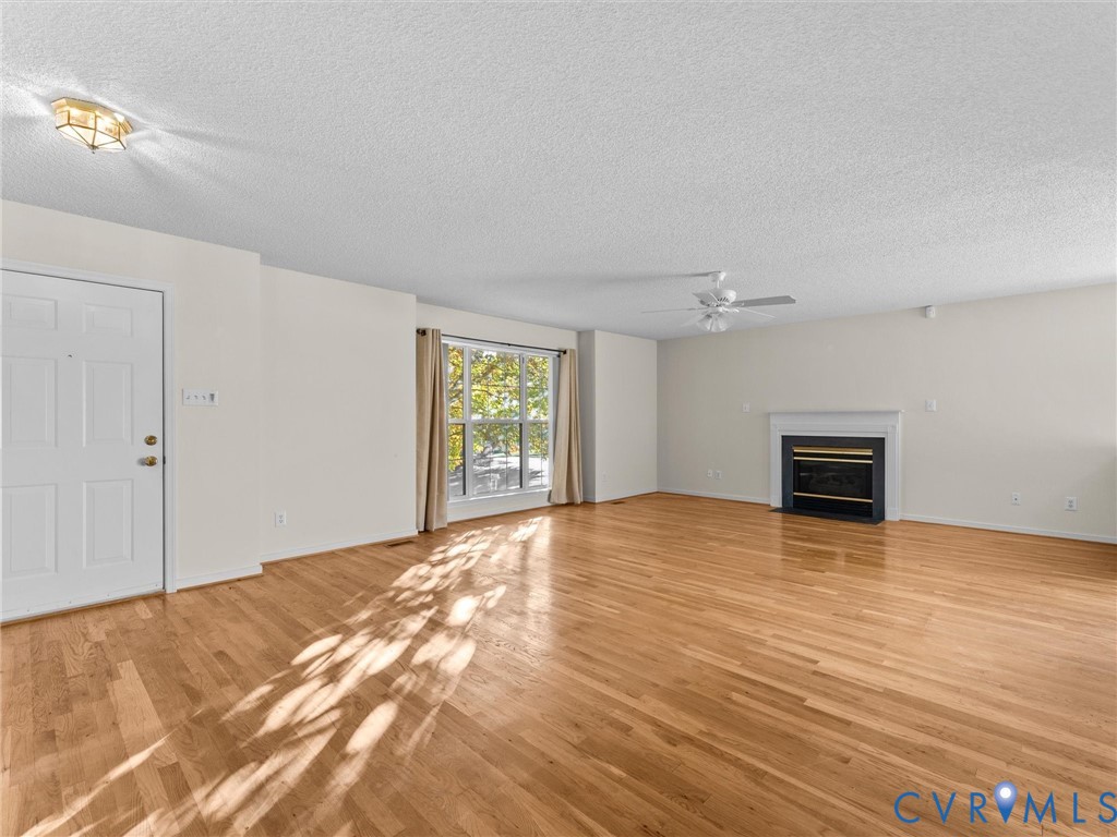 Living area featuring wood-finish flooring, a fireplace with a white mantel, a ceiling fan, and large windows