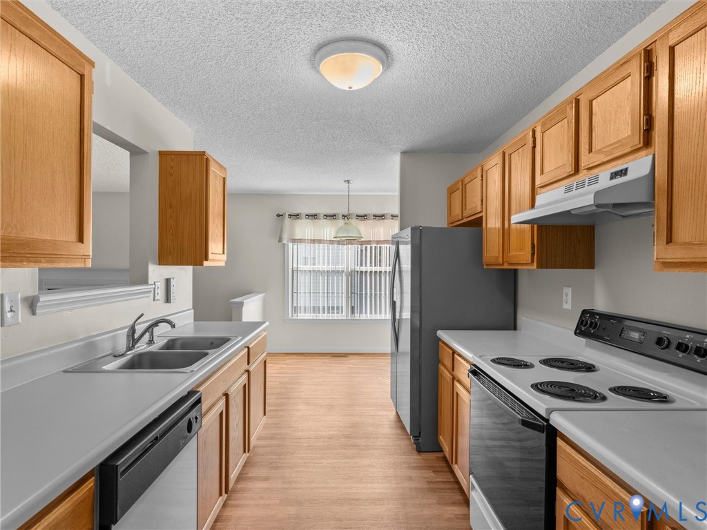 Kitchen featuring wood cabinetry, solid-surface countertops, dual-basin stainless steel sink, and wood-finish flooring