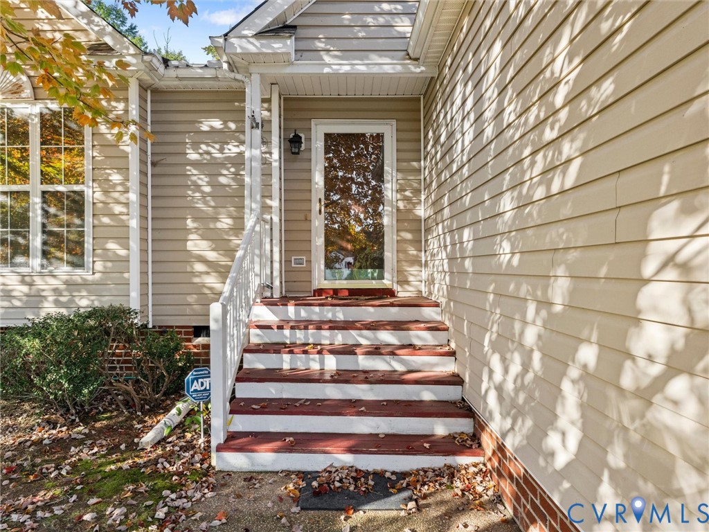 Exterior entrance featuring light-toned horizontal siding, brick masonry base, white railing, and multi-step wooden staircase