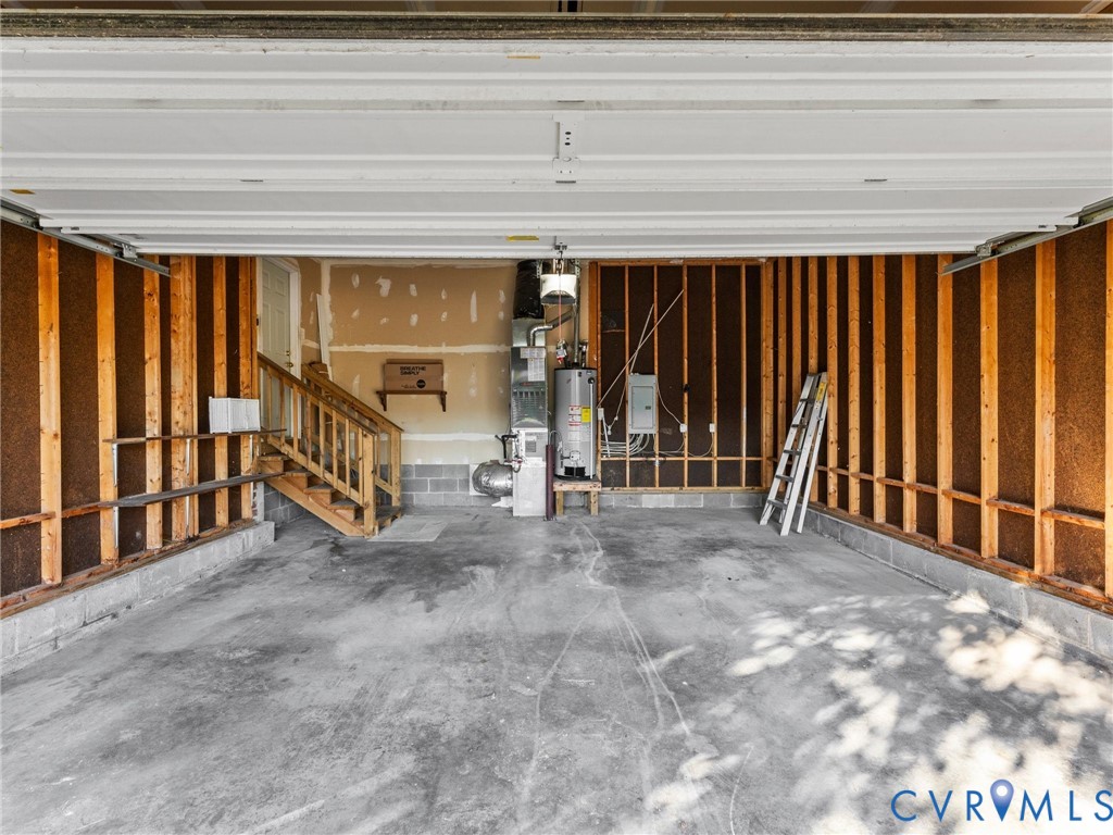 Garage featuring exposed wood framing, concrete flooring, overhead sectional door, water heater, and mechanical furnace system