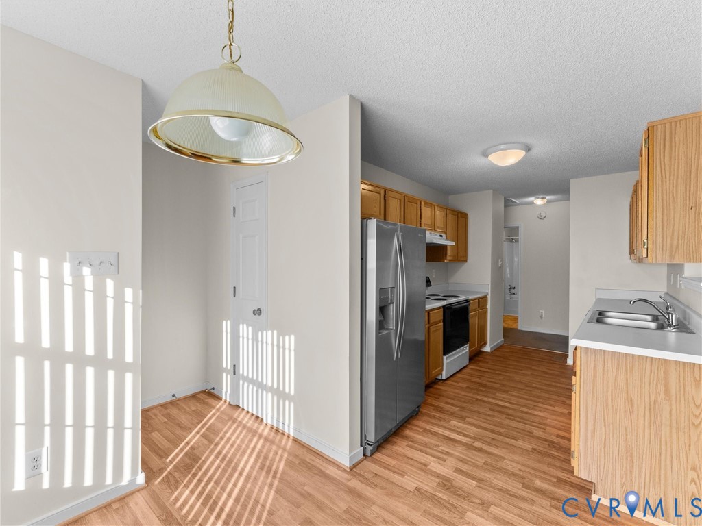 Kitchen featuring wood-finish flooring, stainless steel side-by-side refrigerator, light-tone cabinetry, and a dome-style pendant light fixture