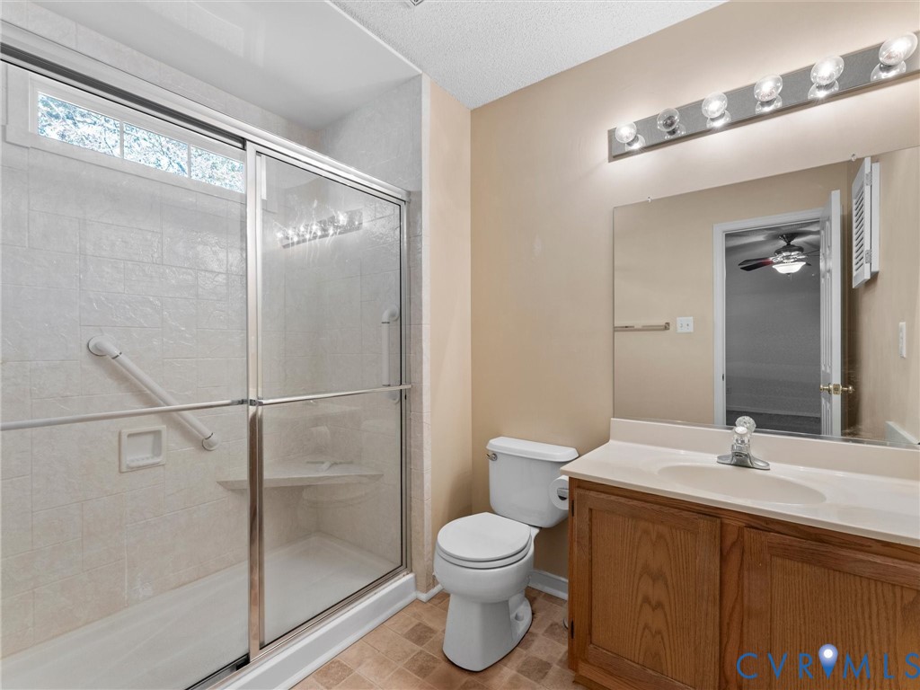 Bathroom featuring a walk-in shower with sliding glass doors, built-in corner bench, and integrated grab bar, complemented by a wood-finish vanity with an oval basin and a large wall-mounted mirror