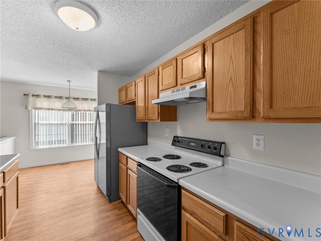 Kitchen featuring wood cabinetry, solid surface countertops, a stainless steel refrigerator, and an electric range with an integrated ventilation hood