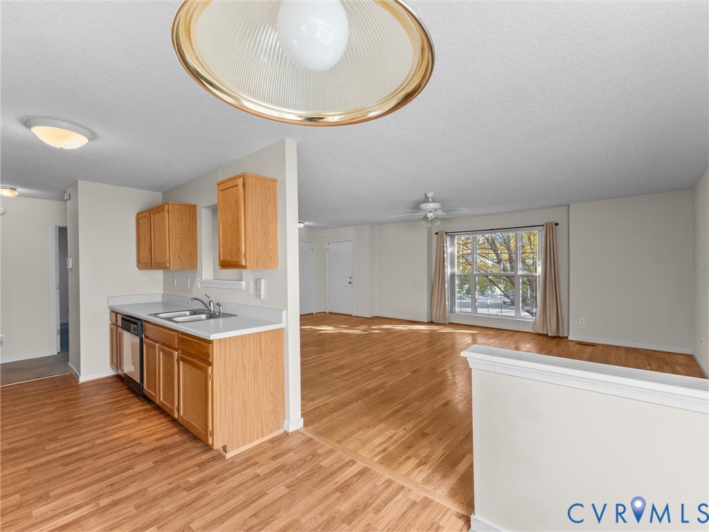 Kitchen featuring wood-finish cabinetry, solid surface countertops, and dual-basin stainless steel sink, complemented by wood-finish flooring and a multi-light ceiling fixture