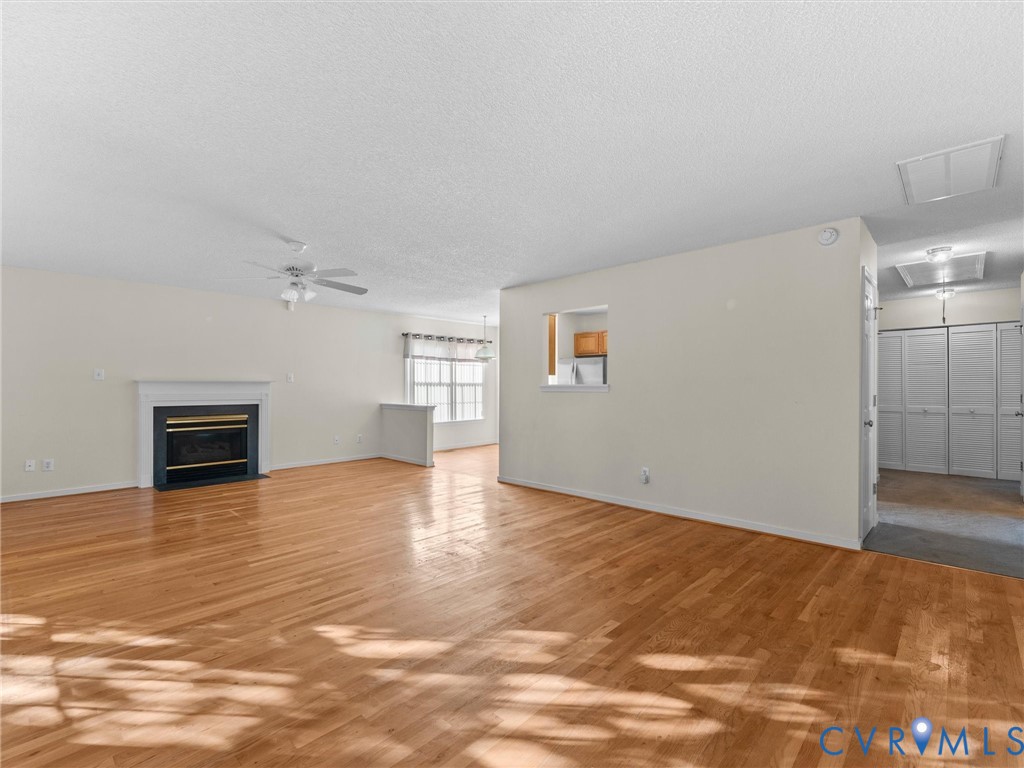 Living area featuring wood-finish flooring, a fireplace with a mantel, a ceiling fan, and multi-panel louvered closet doors