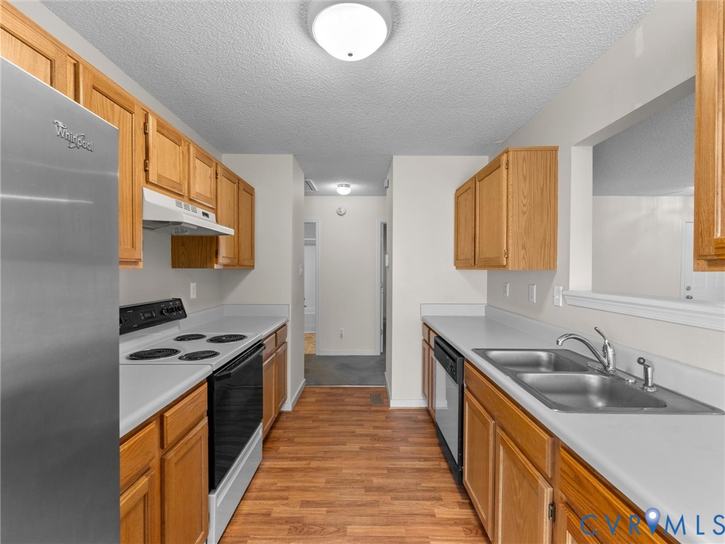 Kitchen featuring wood-finish cabinetry, stainless steel refrigerator, white electric range with hood, double basin stainless steel sink, and wood-finish flooring