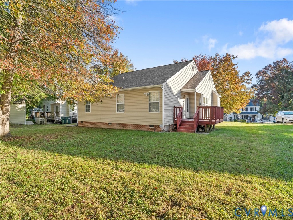 Single-story exterior featuring light-toned horizontal siding, a raised wood-tone deck, a gabled roofline, and a brick foundation perimeter