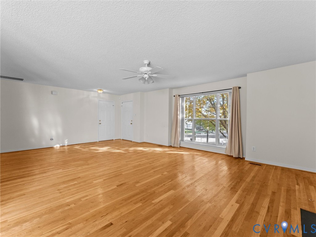 Spacious interior featuring wood-finish flooring, a ceiling fan with integrated lighting, and a large multi-pane window