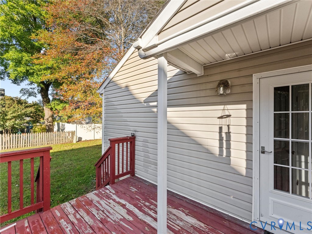 Exterior deck with red-painted wood planks and railings, light-colored horizontal siding, and white-trimmed glass-pane door