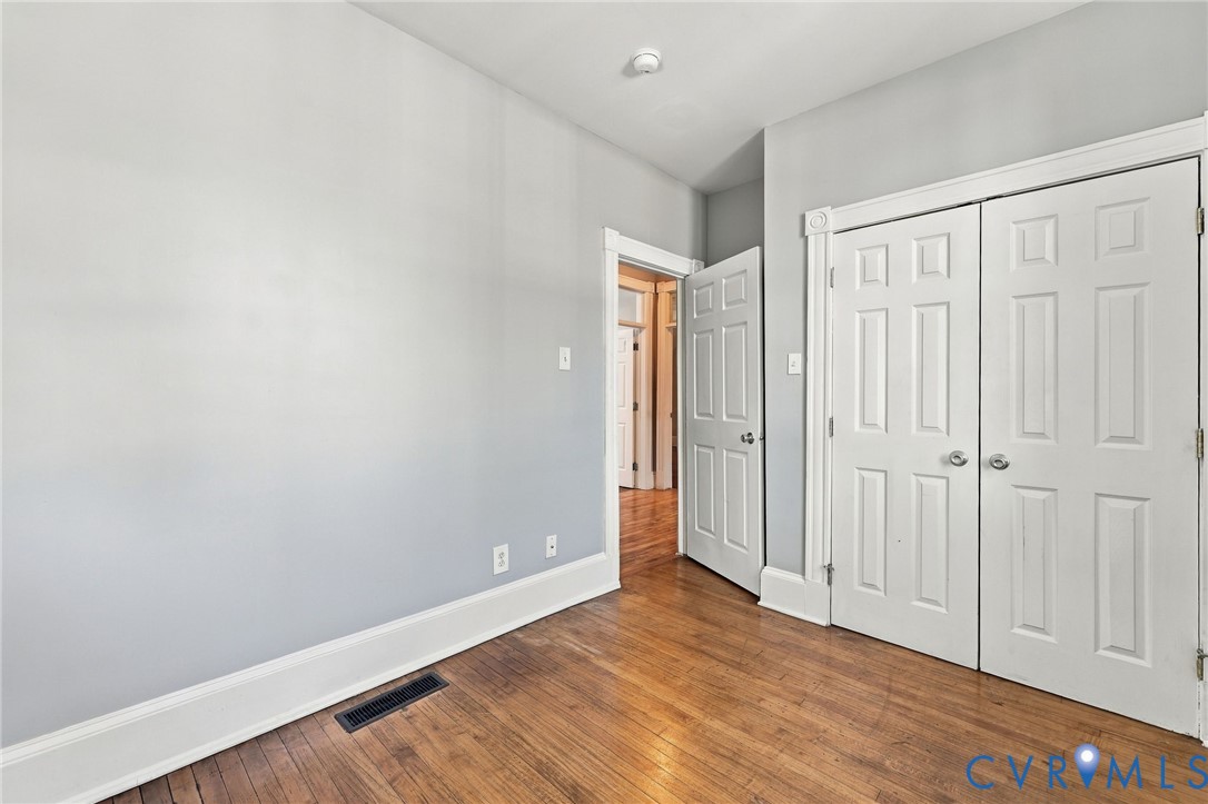 Room featuring wood-finish flooring, white six-panel interior doors, and double-door closet cabinetry with polished chrome hardware