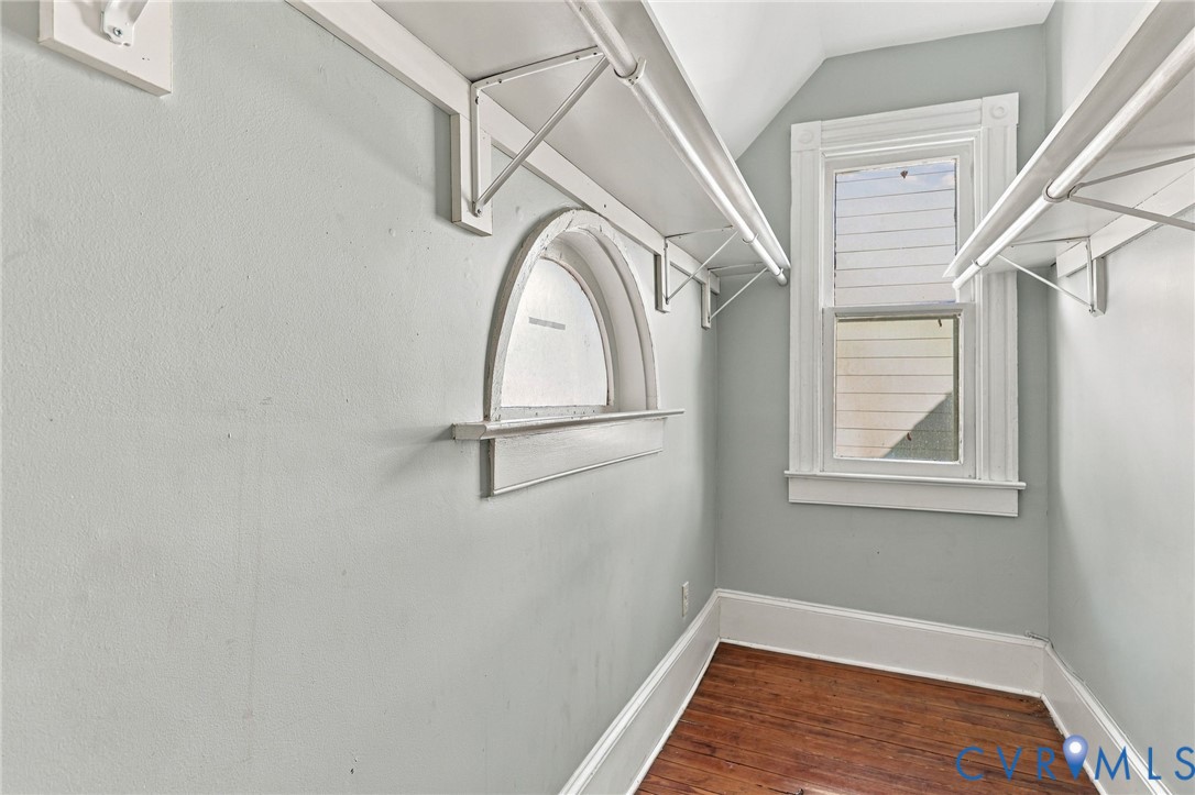 Storage area featuring wood-finish flooring, a double-hung window, a decorative arched window, and white built-in shelving