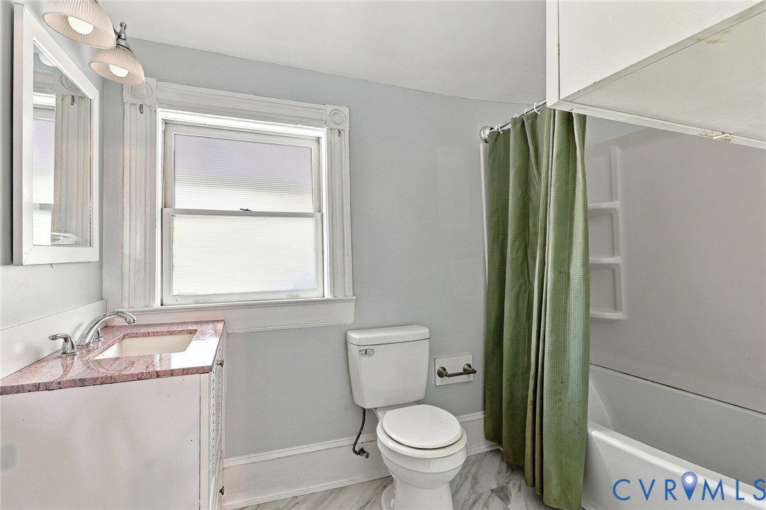 Bathroom featuring a single-sink vanity with stone countertop, window with decorative trim, and combination tub and shower with integrated shelving