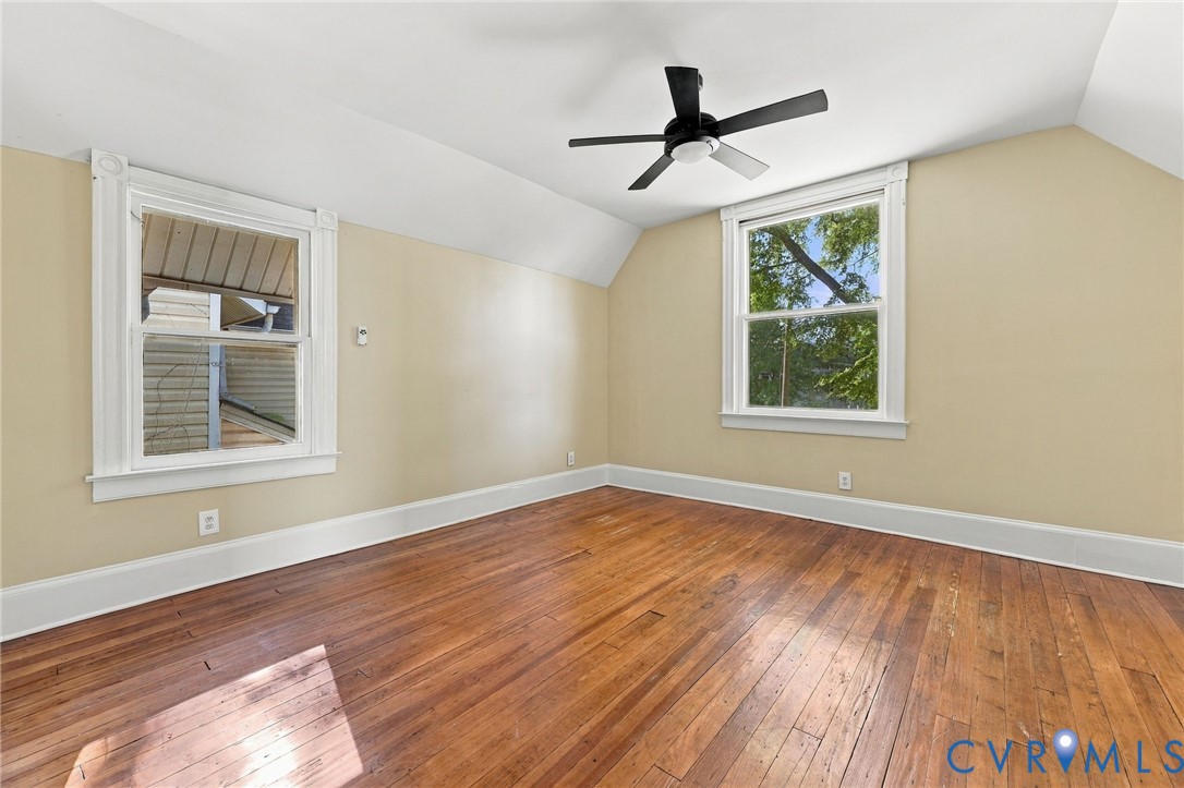 Room featuring wood-finish flooring, dual windows with white casings, and a black ceiling fan