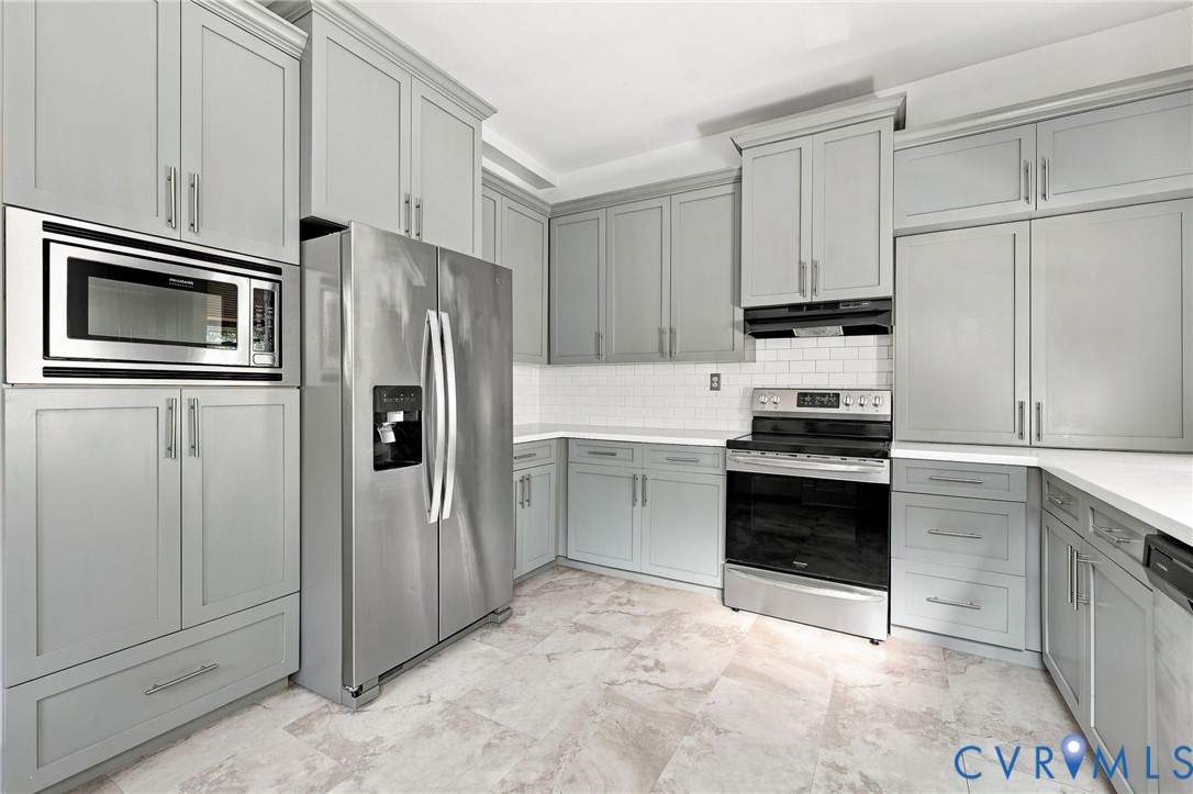 Kitchen featuring grey Shaker-style cabinetry, stainless steel appliances including a built-in microwave and range, white subway tile backsplash, and stone-finish tile flooring