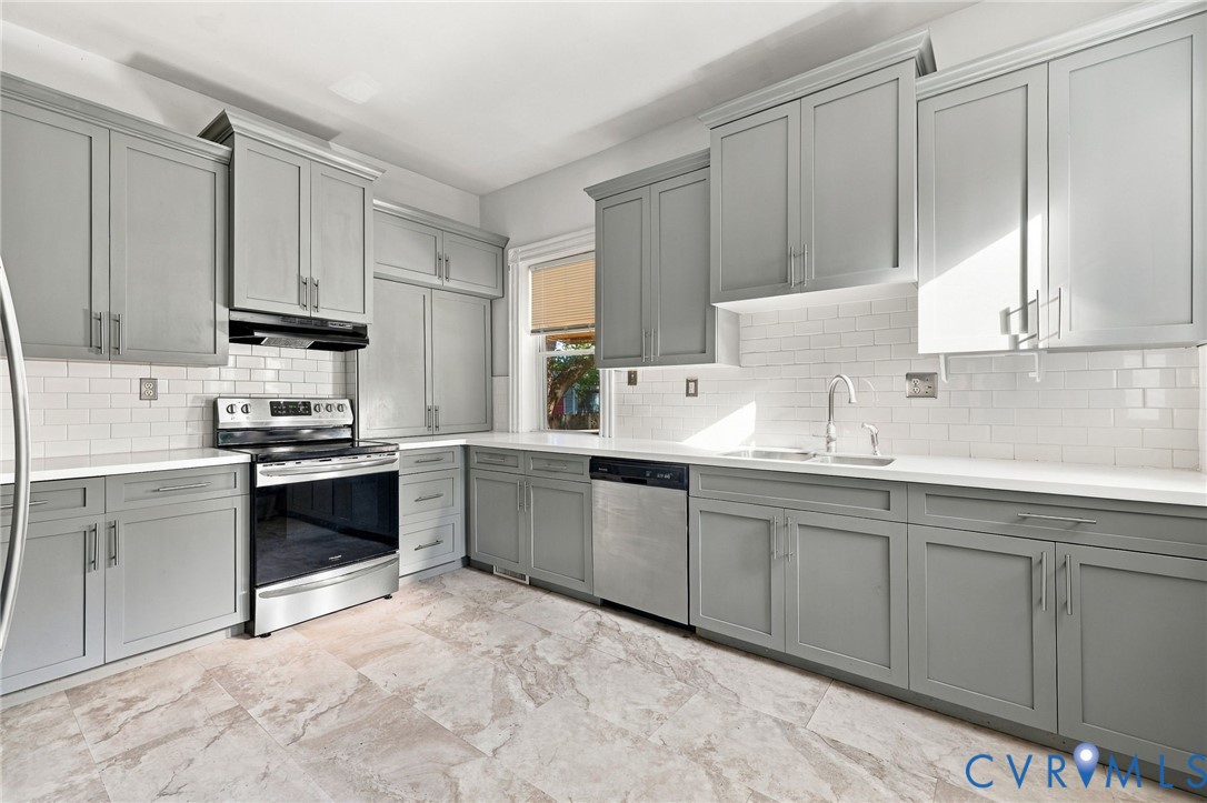 Kitchen featuring shaker-style cabinetry, stainless steel appliances, white subway tile backsplash, solid-surface countertops, and stone-finish flooring