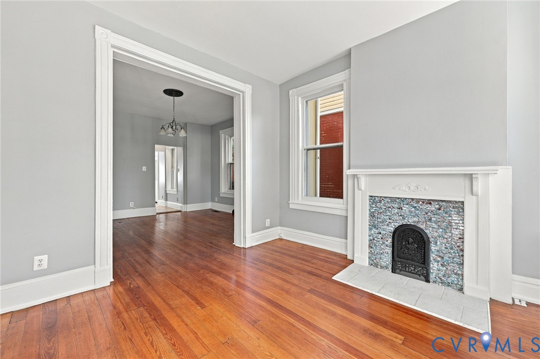 Living area featuring wood-finish flooring, a fireplace with decorative tile surround and white mantel, and wide doorway trim