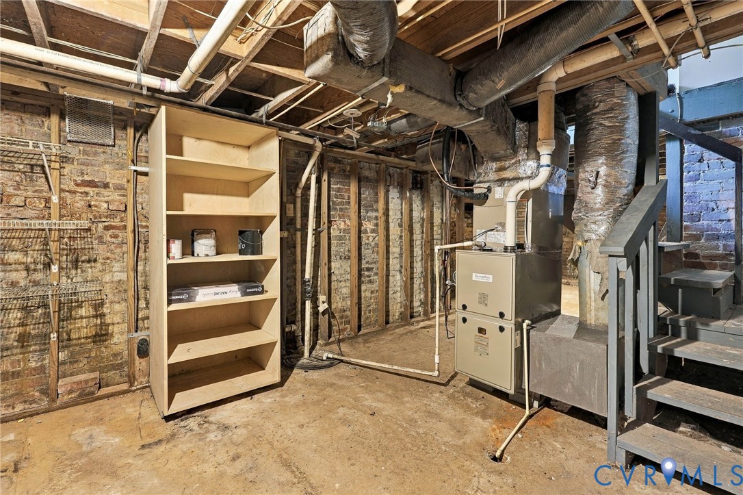 Unfinished basement area featuring exposed brick walls, concrete flooring, built-in shelving, and a gas furnace