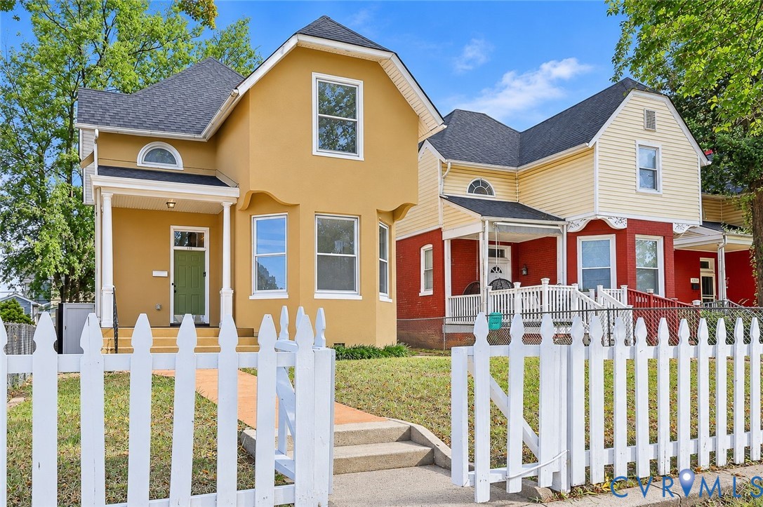 Multi-gabled exterior featuring lap siding and stucco finishes, covered front porches with architectural columns, and a perimeter white picket fence Multi-gabled exterior featuring lap siding and stucco finishes, covered front porches with architectural columns, and a perimeter white picket fence
