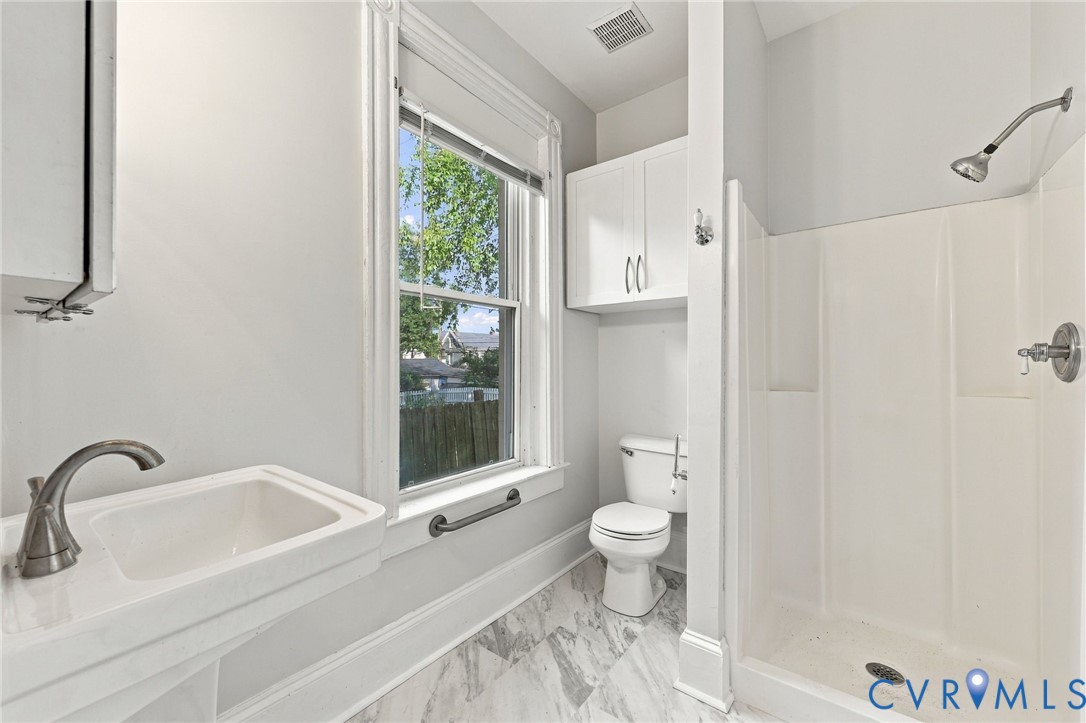 1st floor Bathroom : Wall-mounted pedestal sink with high-arc faucet, tiled stall shower, porcelain toilet, and overhead built-in cabinetry, finished with patterned tile flooring