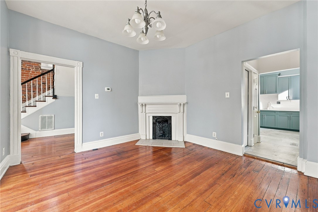 Wood-finish flooring, central fireplace with a classic mantel, arched five-light chandelier, and decorative door casing