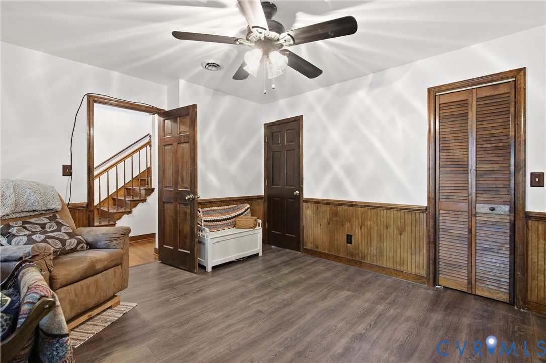 Wood-finish flooring, wood wainscoting, solid-wood six-panel doors, louvered closet doors, and ceiling fan with integrated lighting