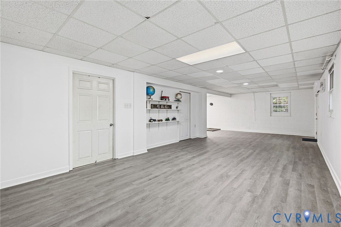 Interior space featuring wood-finish flooring, white walls, recessed ceiling lighting, a grid-pattern drop ceiling, and built-in wall shelving