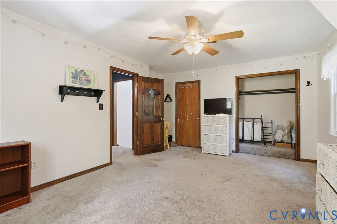 Room featuring neutral carpeting, a central ceiling fan with integrated lighting, solid wood-finish doors with stained trim, and a built-in closet with an open header