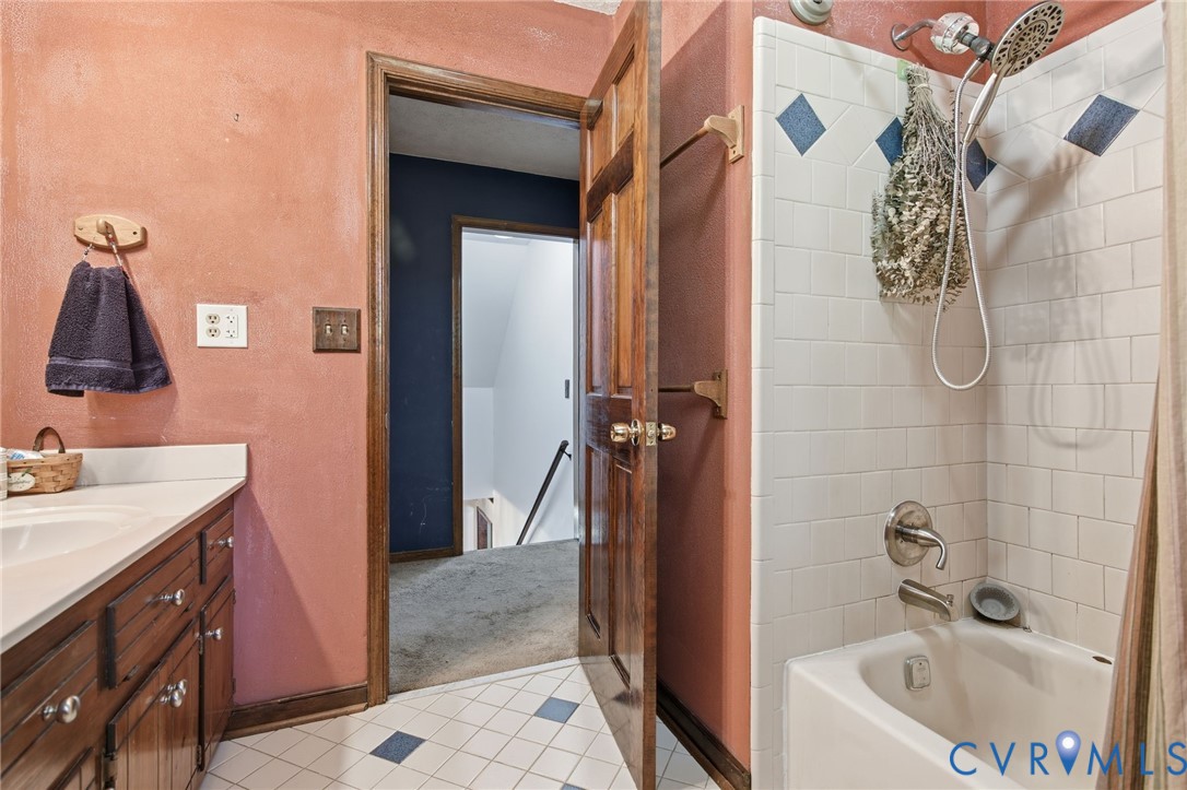Bathroom featuring a vanity with integrated sink, white subway tile shower surround with decorative accent diamonds, porcelain tub, and wood-finish cabinetry