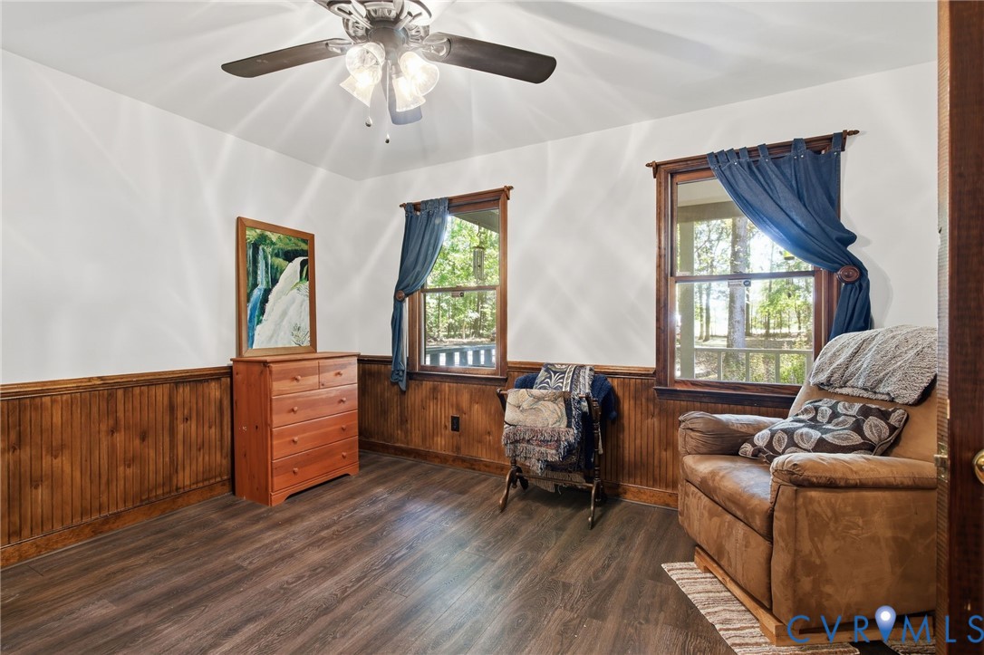 Interior room featuring wood-finish flooring, wood wainscoting, dual windows, and an attached multi-light ceiling fan