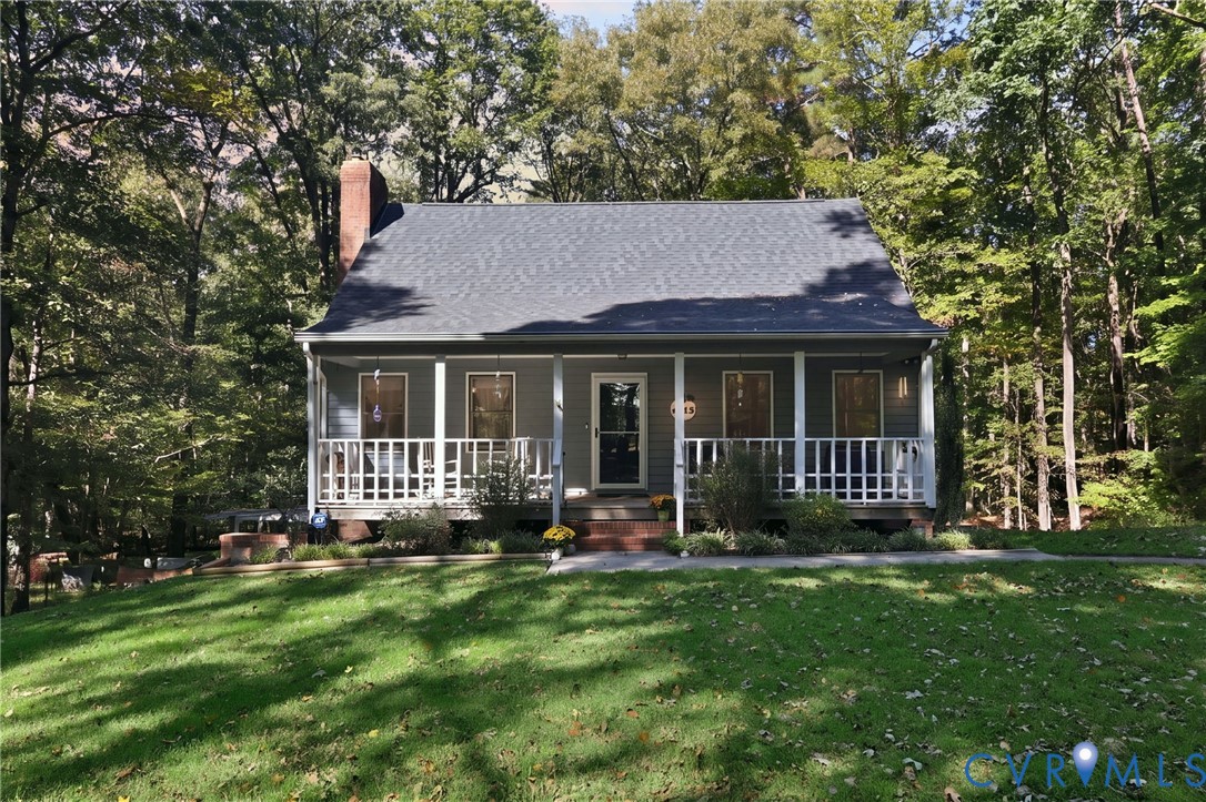 Single-story residence featuring a covered front porch, lap siding, a pitched shingle roof, an exterior brick chimney, and a mature treed lot