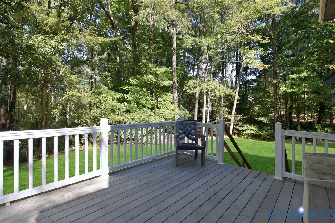Elevated wood-finish deck with white railings, mature trees, and open lawn space
