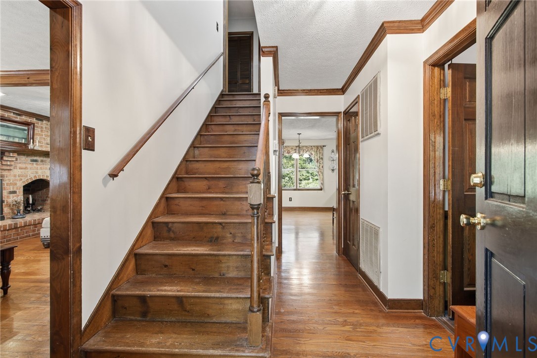 Foyer featuring wood flooring, a wood staircase with a matching handrail and baluster, crown molding, and stained wood door trim